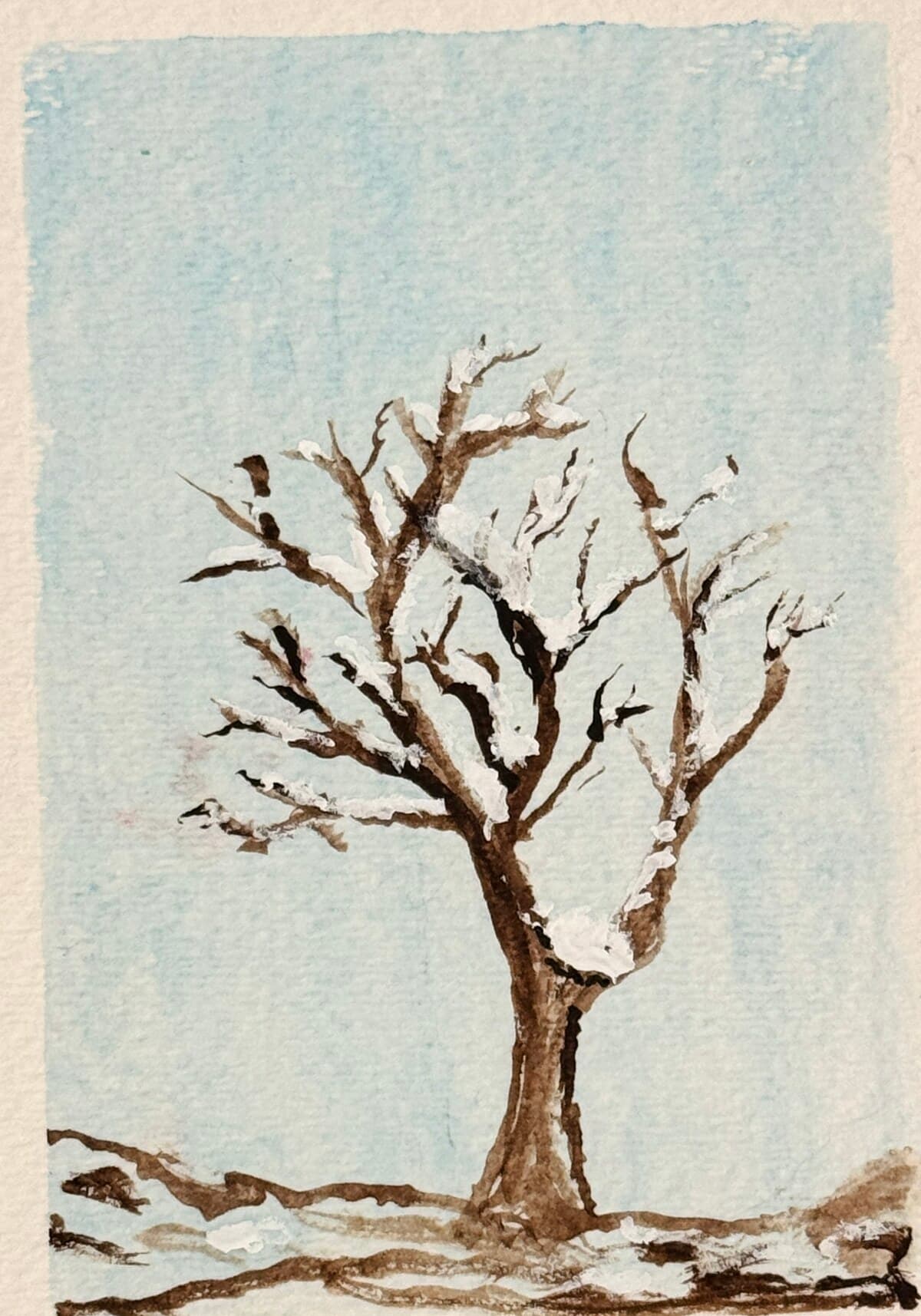 Watercolor of a lone bare tree dusted with snow against a pale blue winter sky